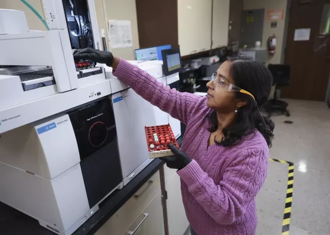 Person in lab, putting little vials with red and light blue lids into a large machine.