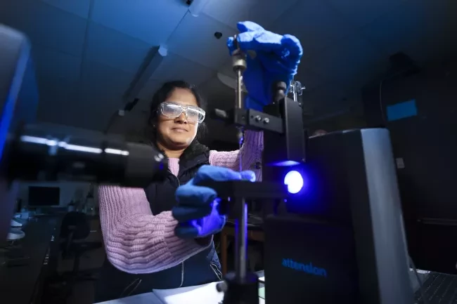 Person in a dark lab, using two hands to put a slide in front of a blue light.